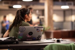 Laptop of security researcher covered customer stickers. Young woman watching intently.